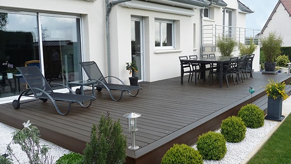 Mørkebrun terrasse med havebord, havestole og lænestole og planter. 